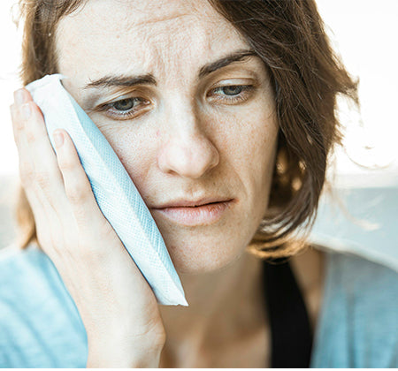 Older woman experiencing jaw pain putting ice on her face